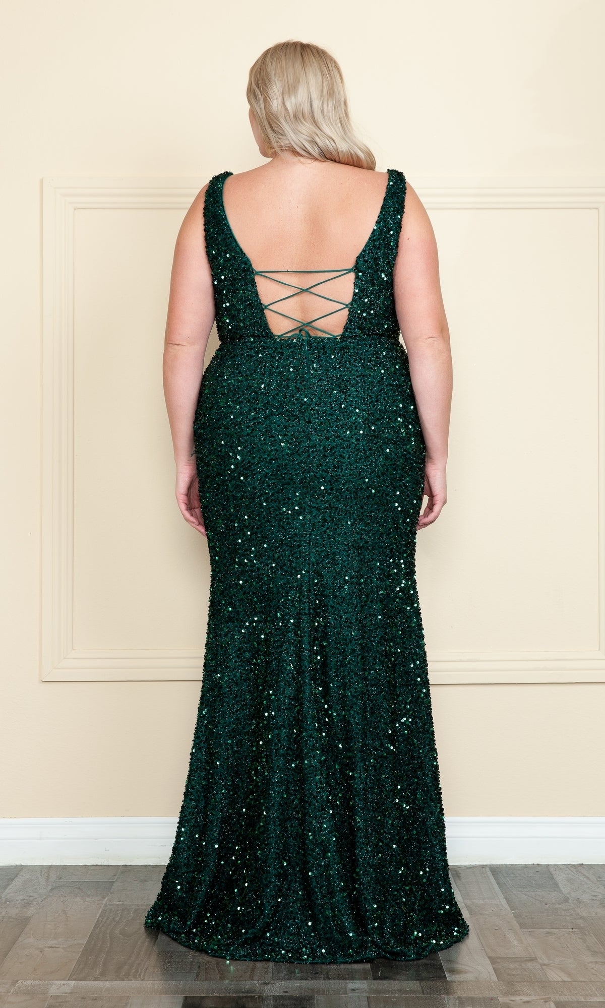 A woman wears the Plus-Size Sleeveless Long Sequin Prom Dress W1126 in dark green, featuring a low open back and crisscross straps, while standing with her back to the camera.
